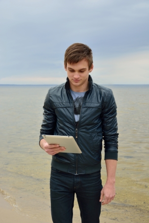The young man is looking on a tablet in front of sea の写真素材
