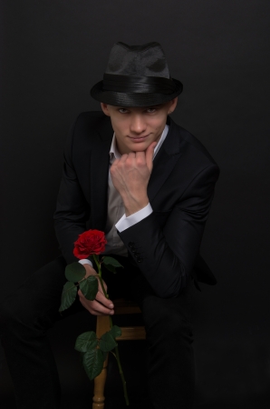 A young man with a rose  Handsome young man in a black suit and hat on a black background and holding a rose の写真素材