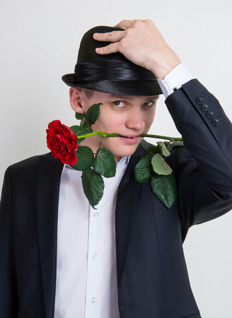 A young man with a rose  Handsome young man in a black suit and hat, sitting on a white and holding a rose の写真素材
