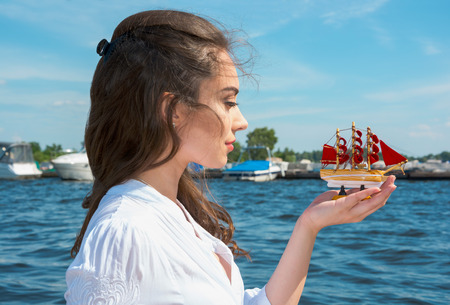 Girl holds a small ship with red sails   Modern Assol near the water の写真素材
