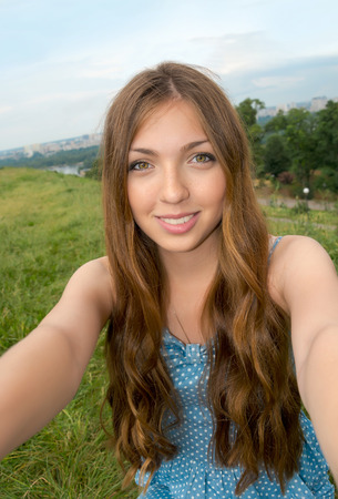 Beautiful girl taken picture of herself, selfie. Young woman with long hair photographed herself in front of the cityscape.の写真素材