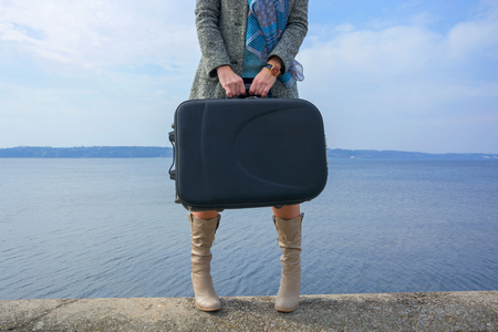 Female legs in a boots and with a suitcase in front of the seaの写真素材
