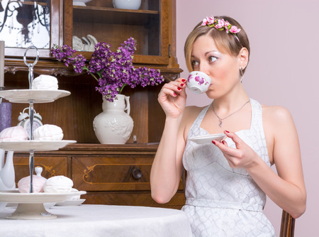 Young girl in a retro style wedding dress is drinking tea near a cupboardの写真素材
