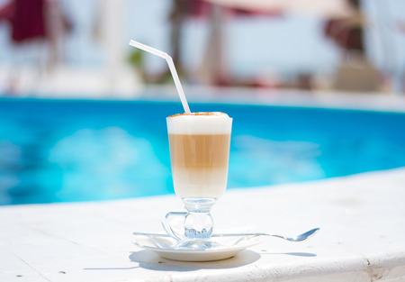 Glass with a coffee latte by the poolの写真素材