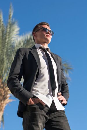 Man in sunglasses and in a jacket at the palm tree in summer timeの写真素材