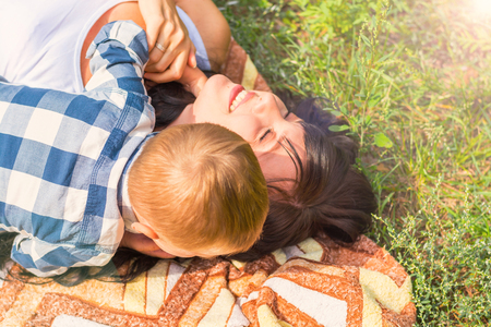 Mom and her little son indulge and have fun on a plaid on the grass in the park at sunny dayの写真素材