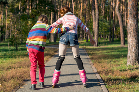 The boy helps the girl to roller-skate in the park. Brother supports his sister, who is riding on the rollers.の写真素材