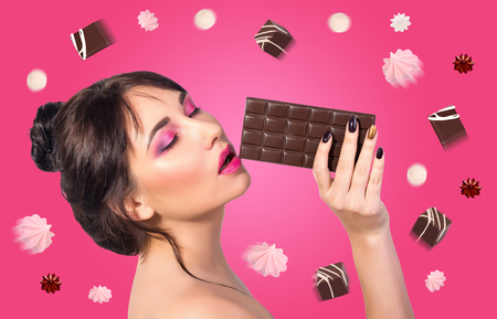 Woman and chocolate. Beautiful young woman is eating chocolate on a pink background. Sweets fly around a girl who eats chocolate. Conceptの写真素材