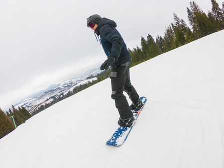 A young man in sports glasses is riding a snowboard in the mountains in Transcarpathia, Ukraine.の写真素材