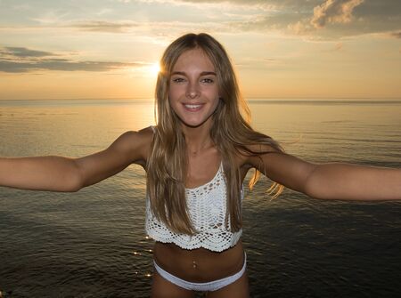 Beautiful happy young woman makes selfie at the sea background at the sunsetの写真素材