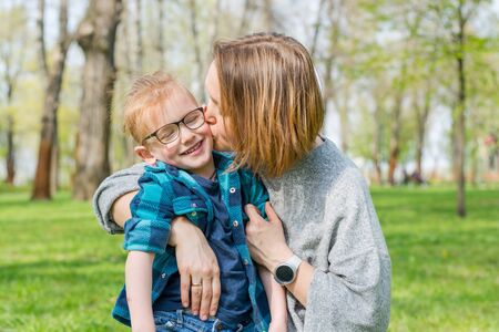 Mom kisses her little boy in glasses in the park on the grass in spring. の写真素材