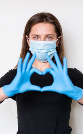 Young woman in medical mask and gloves shows a heart sign by hands. Quarantineの写真素材