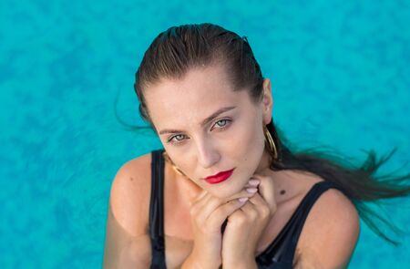 Portrait of a beautiful young woman in the pool. Woman is relaxing in a pool. Young woman is swims in the black swimsuitの写真素材