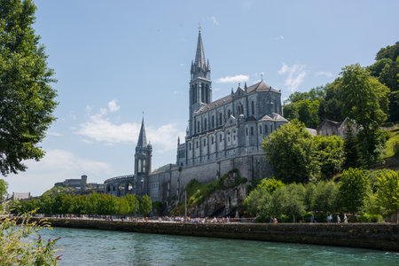 editorial. July, 2022. Lourdes, France. View of the river Gave de Pau and the Basilica of the Holy Rosary in Lourdes, France. The Sanctuary at Lourdes. A gilded cross crowns the dome of the Basilica of the Holy Rosary.のeditorial素材