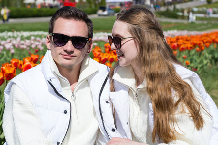 Young beautiful smiling couple, on the background of a field of colorful tulips. Guy and girl are...