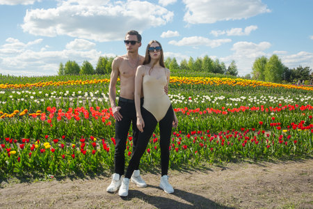 A beautiful young couple, fashion models stands in sportswear at the background of a field of colorful tulips. A guy hugs a girl.の写真素材