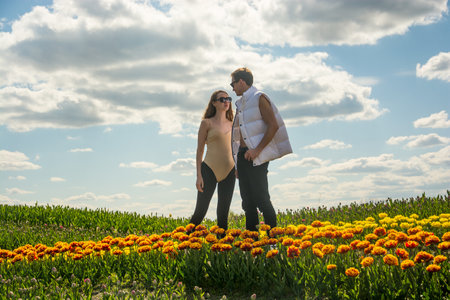 A beautiful young couple, fashion models stands in sportswear at the background of a field of colorful tulips. A guy looks at the girl.の写真素材