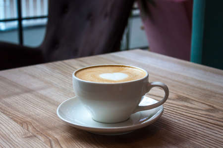 White cup of cappuccino with love art foam on light wooden table, heart shape Valentine's concept.の写真素材