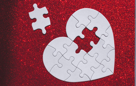 White heart shaped puzzle with missing part on red sparkle background.の写真素材