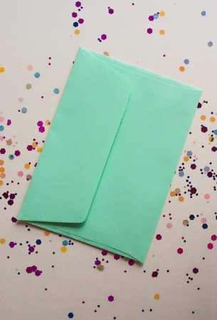 Soft green envelop on light festive background with sparkles. Flat lay style.