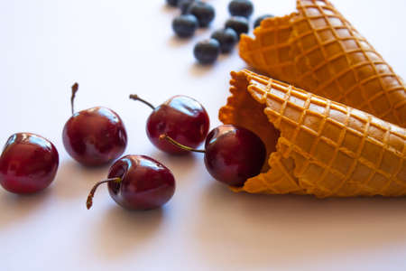 Ice cream waffle cones with blueberries and sweet cherries, minimal side view.の写真素材
