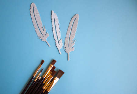 Set of brushes for painting and silver quills on blue background, flat lay.の写真素材
