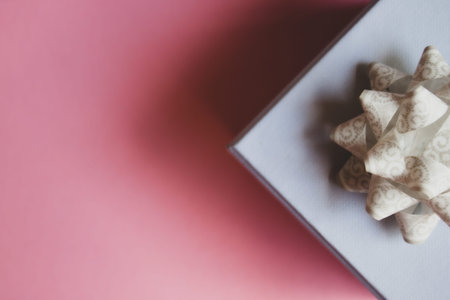 Gift box with white bow on soft pink background. Flat lay. Festive concept.の写真素材