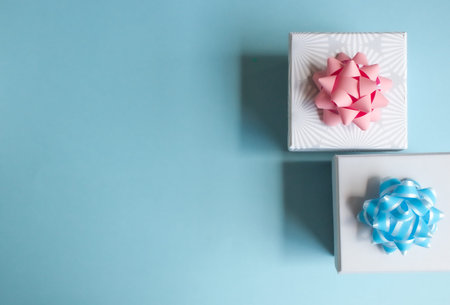 Two light gray gift boxes with light bow on blue background. Festive concept.