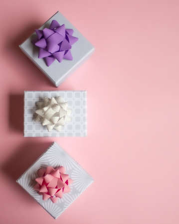 Three light gray gift boxes with colorful bows on pink background. Festive concept. Flat lay.の写真素材