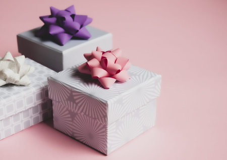 Three light gray gift boxes with colorful bows on pink background. Festive concept.
