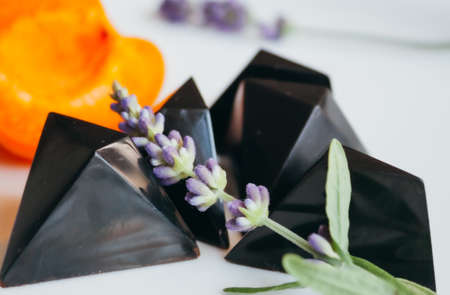 Molded dark chocolate pralines in black color with lavender and apricot on white background.の写真素材
