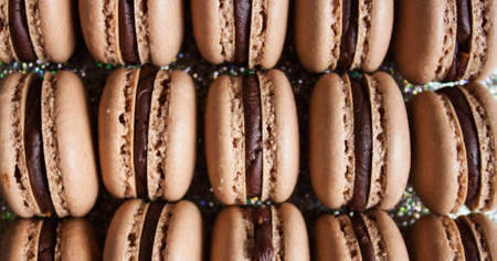 Many dark chocolate macarons on sparkling background.の写真素材