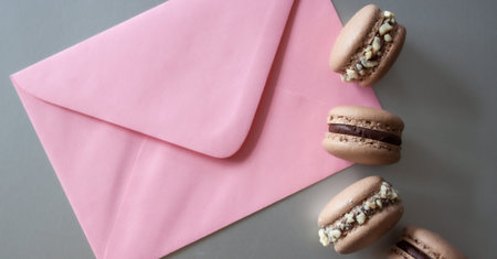 Pink envelope and dark chocolate macarons on silver background.