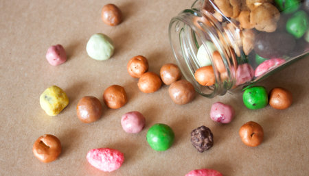 Glass jar full of colorful chocolate handmade gourmet dragee candies on Kraft paper background.