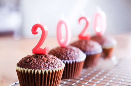 Classic dark chocolate cupcakes with red new year candles on silver baking rack and light wooden background. の写真素材