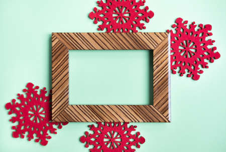Brown shiny wooden frame and Christmas vibrant red snowflakes on mint green background. Festive concept. Perfect backdrop for holidays.の写真素材