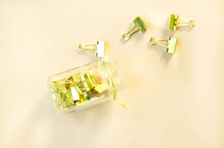 Golden paper clips and glass jar on sunny yellow background. Top view, flat lay. Minimal school or office stationery.の写真素材