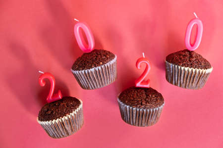 Classic dark chocolate cupcakes with red new year 2020 candles on Christmas happy red background.の写真素材