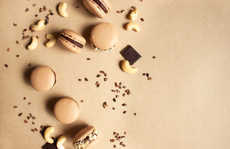 Dark chocolate macarons with cashew nuts and cocoa nibs on caramel color background.の写真素材