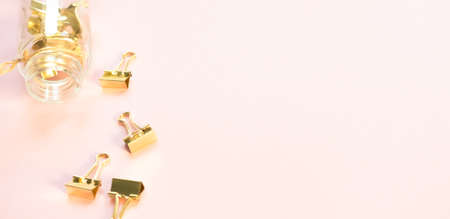 Golden paper clips and glass jar on pink orange background. Top view, flat lay. Minimal school or office stationery.の写真素材