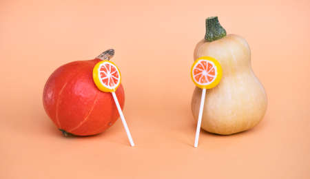 Two multicolored pumpkins and lollypops on peach orange background. Halloween funny holiday concept.の写真素材