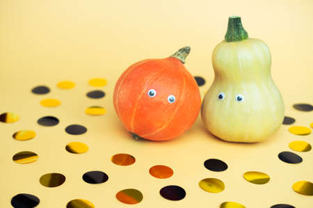 Two multicolored pumpkins and confetti on trendy orange background. Halloween funny holiday concept.の写真素材