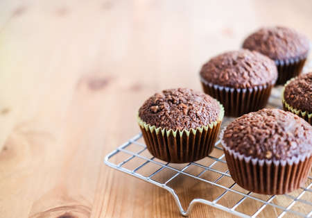 Classic dark chocolate cupcakes on silver baking rack and light wooden background.の写真素材