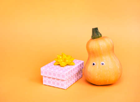 Yellow pumpkins and gift box on trendy orange background. Halloween funny holiday banner concept.の写真素材