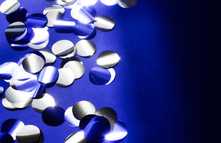 Shiny golden, silver and black confetti on dark blue background. Festive modern concept.
