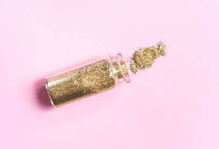 Glass bottle of golden shiny glitter tinsels on pastel pink background. Magic festive concept. の写真素材