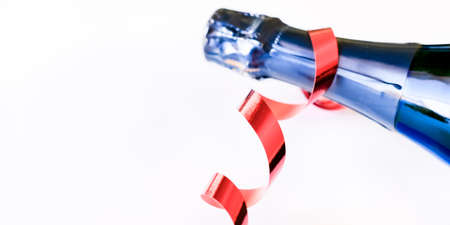 Dark blue bottle of champagne with red ribbon on white background. Festive concept. Flat lay style banner.の写真素材