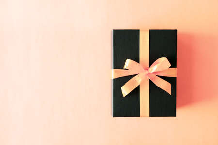 Black gift box with orange bow on pastel coral pink background. Flat lay festive minimal style.の写真素材