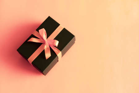 Black gift box with orange bow on pastel coral pink background. Flat lay festive minimal style.の写真素材