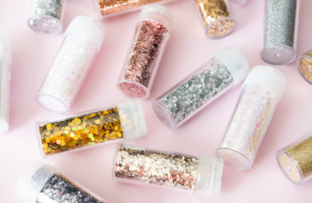 Plastic containers with metallic shiny glitter, Christmas decor set on pastel pink background. Magic...